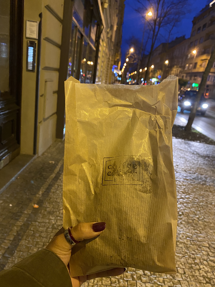 A student's hand holding a bag of banana nut bread to go against the backdrop of a city street at night. 