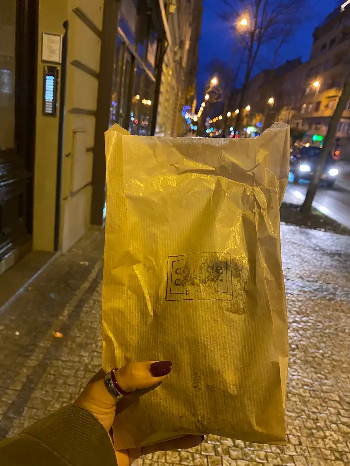 A student's hand holding a bag of banana nut bread to go against the backdrop of a city street at night. 
