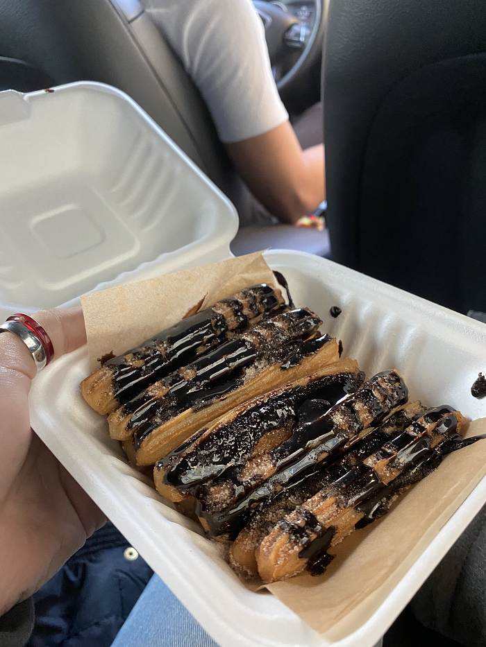 A small takeout container of mini churros covered in cinnamon sugar and hot fudge. 