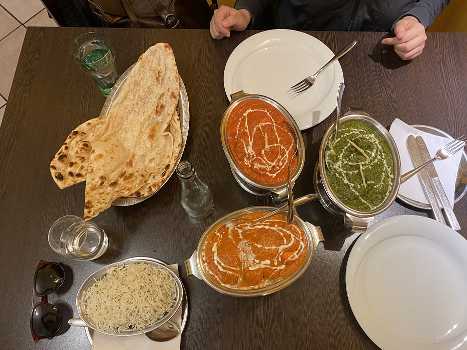 A bird's eye view of a table with three platters of curry, one bowl of rice, and a bowl of naan. 