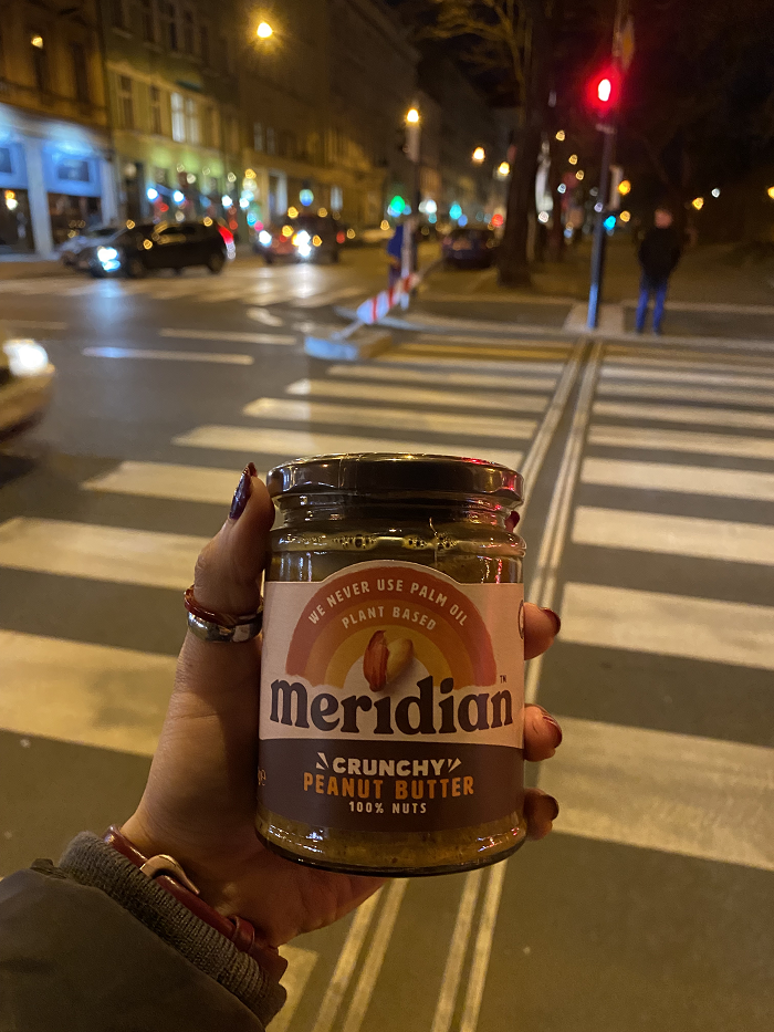 A student's hand holding a jar of crunch peanut butter against the backdrop of a large crosswalk at night. 