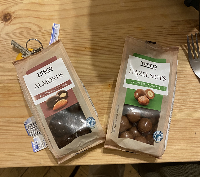 Two small packets of chocolate covered nuts atop a table with keys and a fork.