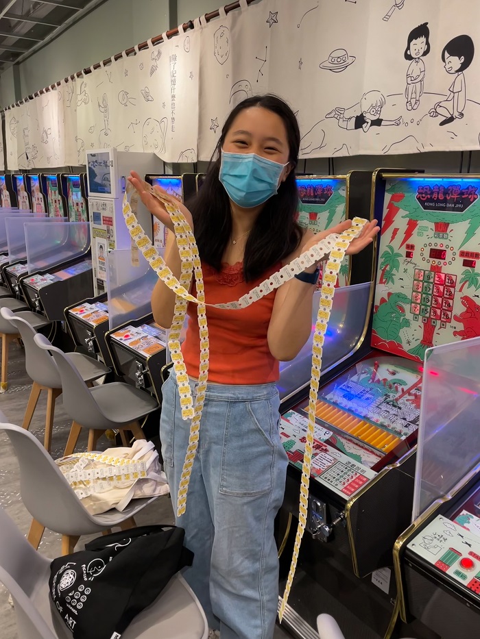 Wendy Zhang holding up arcade tickets with game machines behind her 