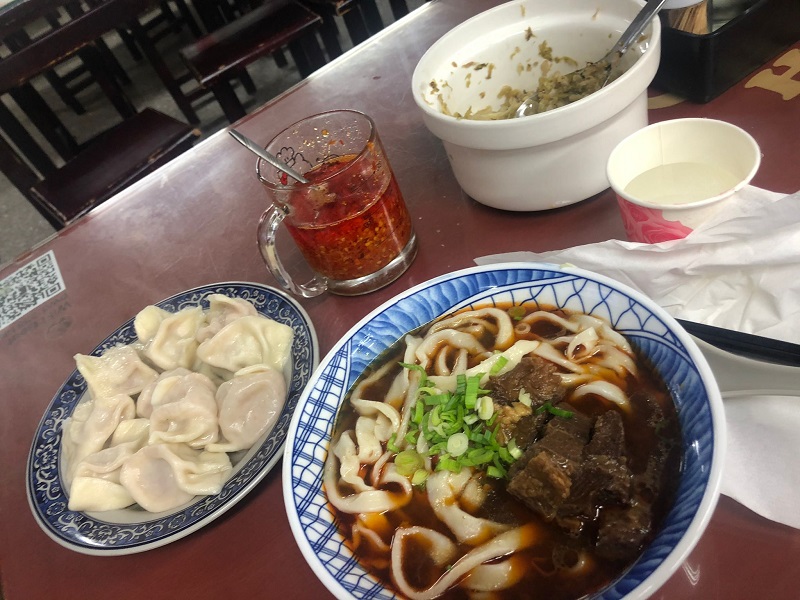 Bowl of beef noodle soup and dumplings on the side