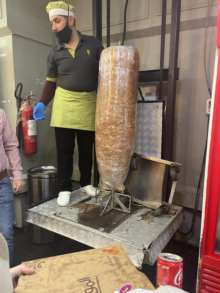 man standing next to shawarma stand