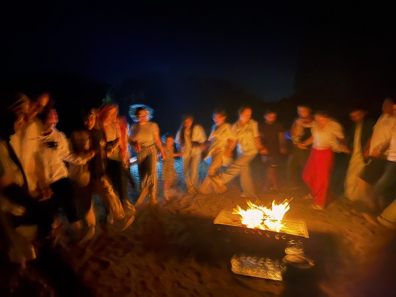 blurry photo of cet students hand in hand dancing around a campfire
