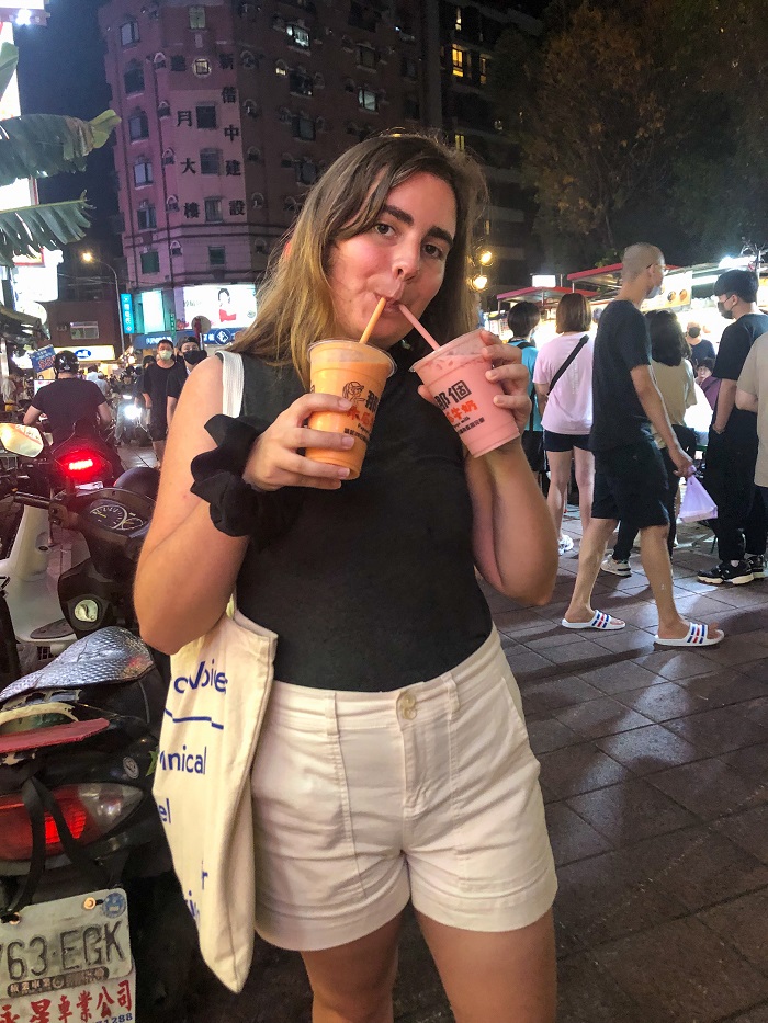 Elissa drinking two different flavors of fruit milk at the night market