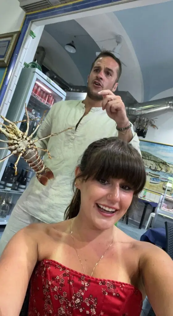 Grace taking a selfie with a man holding a lobster in the background 