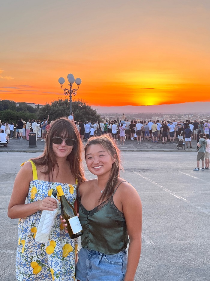 Grace and Anessa posing with bottles of wine in front of sunset