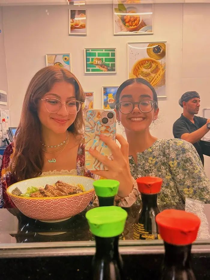 Grace and Genevieve taking a mirror selfie in a ramen restaurant
