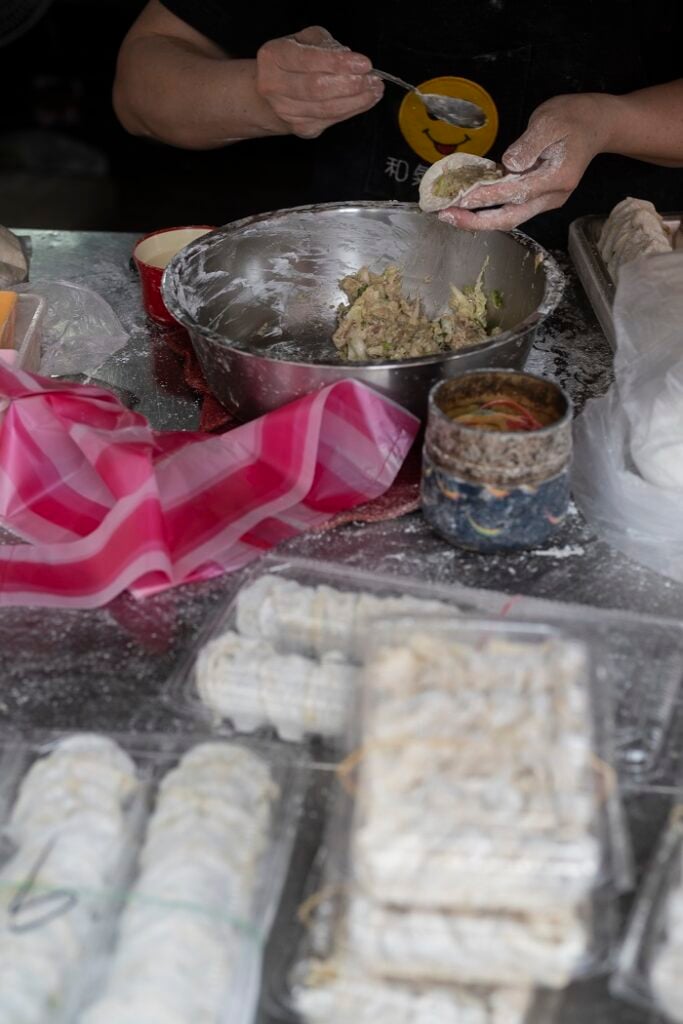 A neighborhood market vendor wrapping dumplings over a metal bowl.