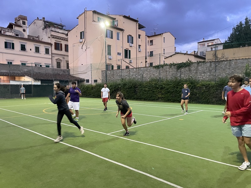 Students running on a soccer field in the middle of Florence, surrounded by residential buildings. 