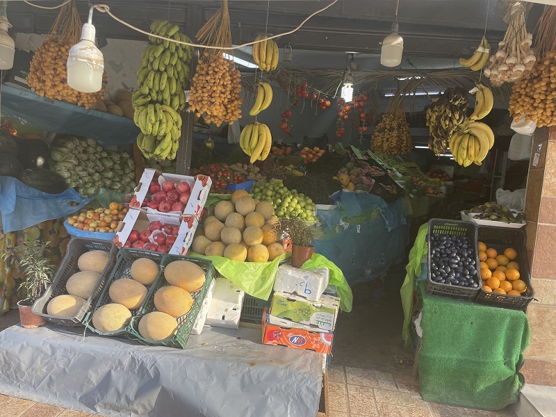 A neighborhood fruit stand with melons, bananas, and oranges all throughout the shop.