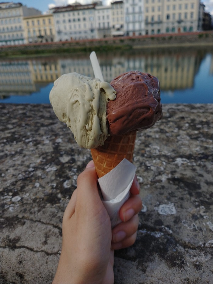Two scoops of melting ice-cream on a cone held in front of Arno River  