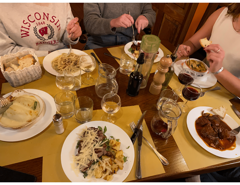 People eating at a dining table with an array of Italian food, wine glasses, and water cups