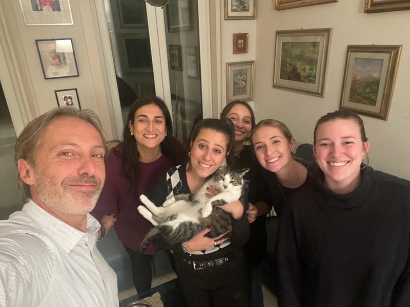 Students and an Italian family smiling with a cat in a living room 