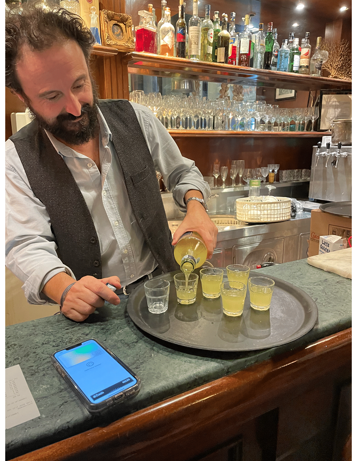 A bartender pouring limoncello into shot glasses in a bar