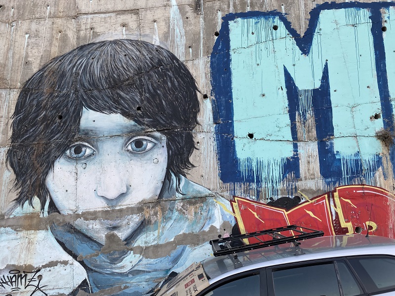 A graffiti of a young boy in blue tones next to some graphic lettering.