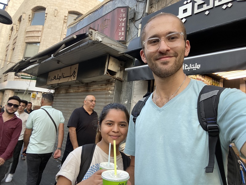 Two students drinking sugarcane juice on a busy sidewalk in Amman.