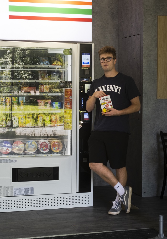 Student leaning against a vending machine and eating chicken broth flavored chips.