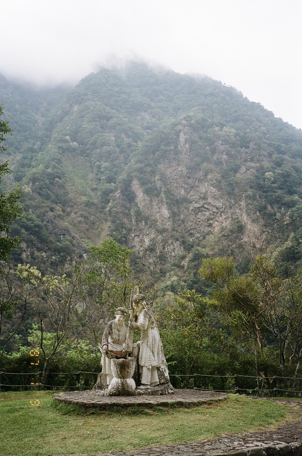A statue of two members of the Truku Tribe against the backdrop of green rock faces.