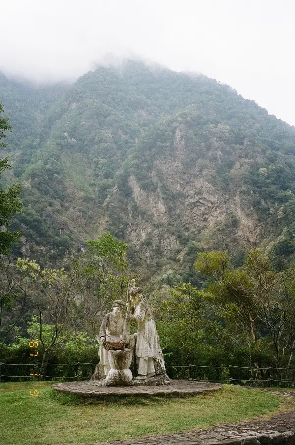 A statue of two members of the Truku Tribe against the backdrop of green rock faces.