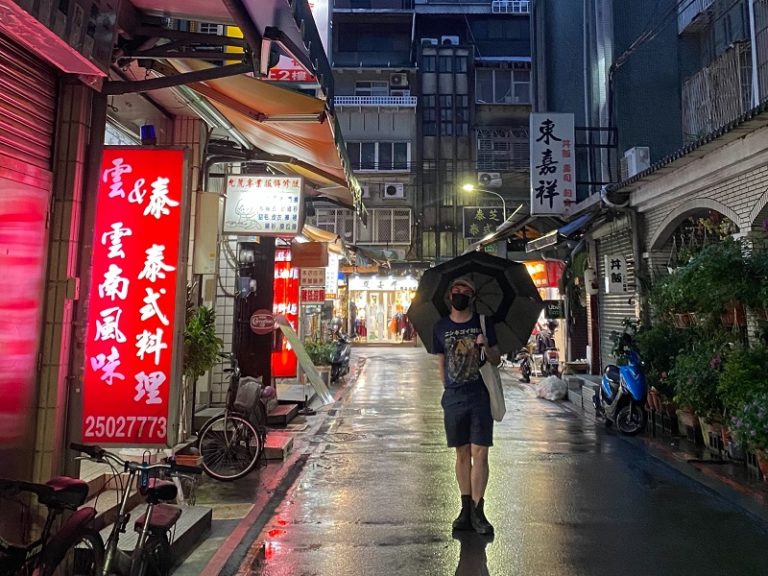 A student standing in the middle of a quiet street at night with an umbrella.