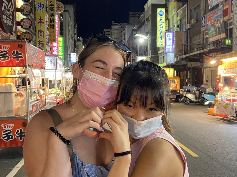 Two students holding their hands together to form a heart at a local night market