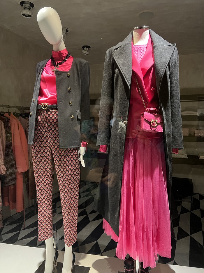 The window of a luxury shop with two mannequins dressed in black and hot pink clothing on Via Tornabouni in Florence 