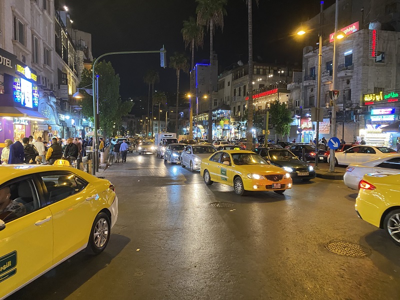 The streets at the heart of West al-Balad at night with many cars, shops, and people