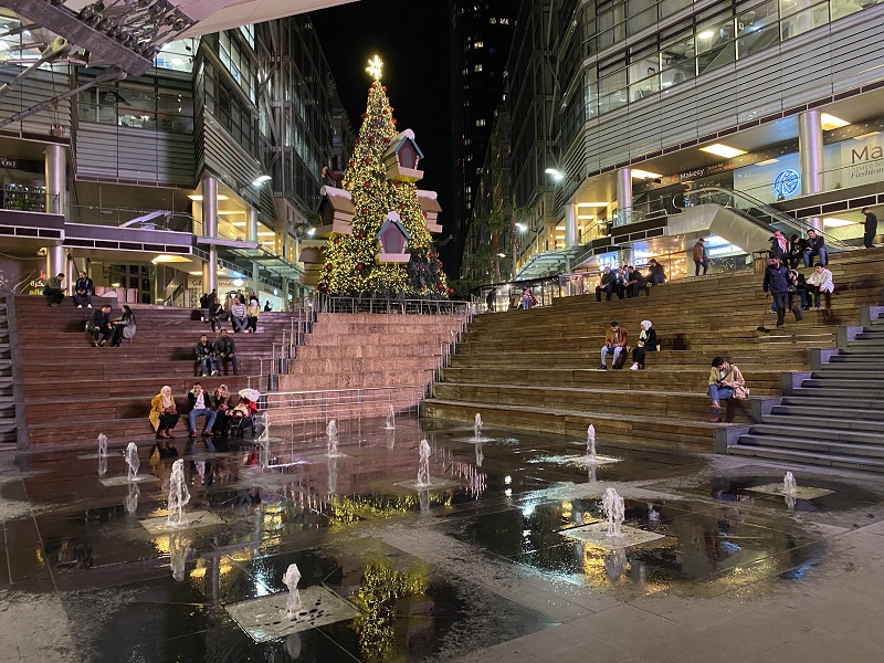 A giant Christmas tree set up at the Boulevard, a walking street right next to Abdali Mall and  people sitting on stairs