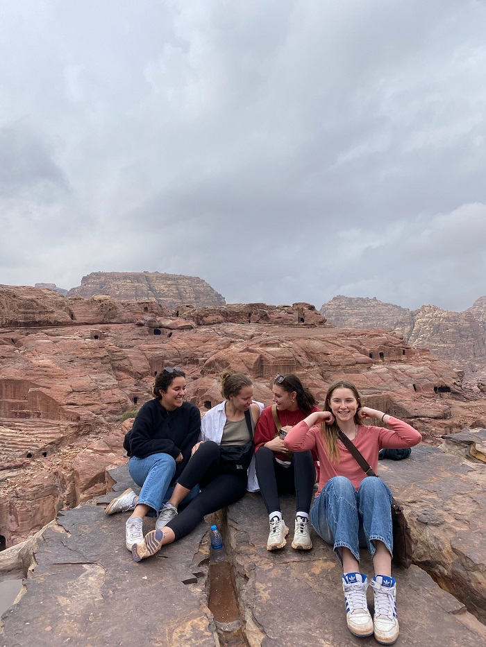 Four female students sitting and smiling on red rocks in Jordan