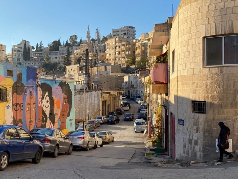 Street view of Amman with some cars parallel parked to the left side against some colorful grafitti.