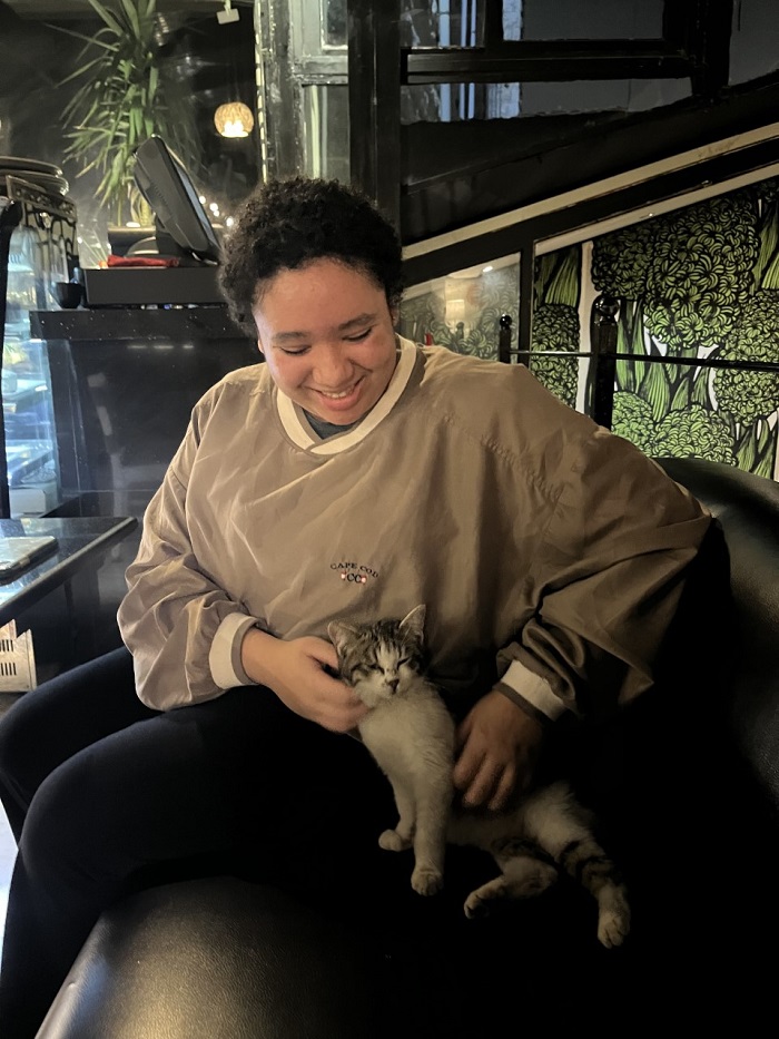 A CET female student smiling and holding a white and grey cat on a sofa in a restaurant 