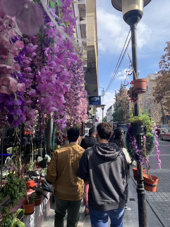 People walking by a shop with lots of purple and green plants on Rainbow Street in Amman, Jordan 