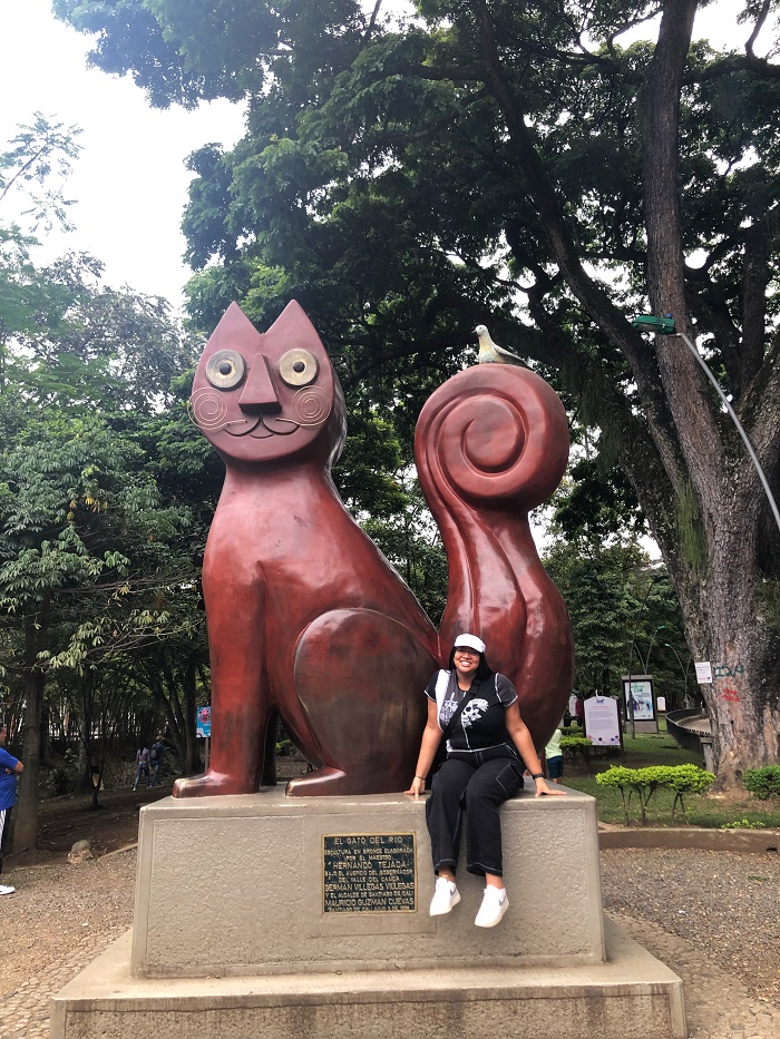 A CET Colombia student in a park in front of a giant red cat statue