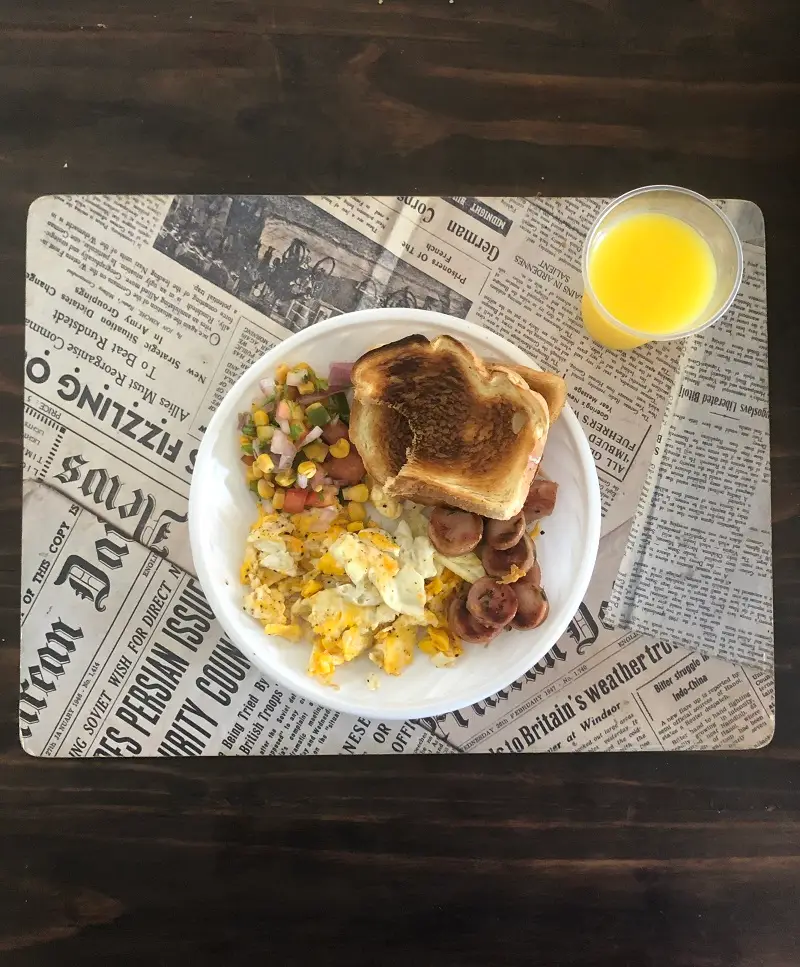 Bread, eggs, vegetables on a plate with a cup of orange juice to the side