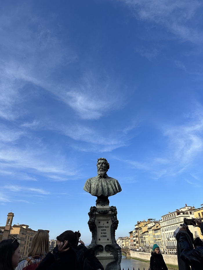 The bust of Benvenuto Cellini on the Ponte Vecchio in Florence surrounded by a couple of people and students