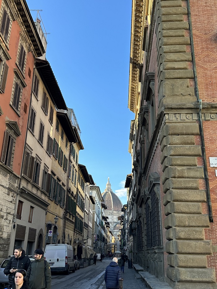 A street with cars and people in Florence with the Duomo in-between buildings