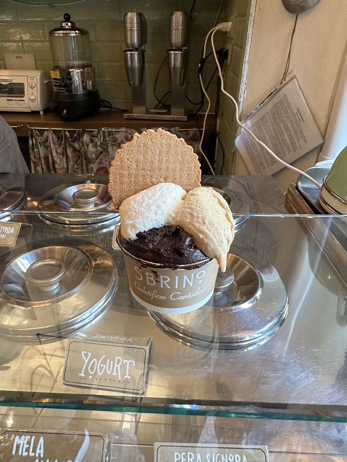Three scoops of gelato in a cup with a waffle cracker