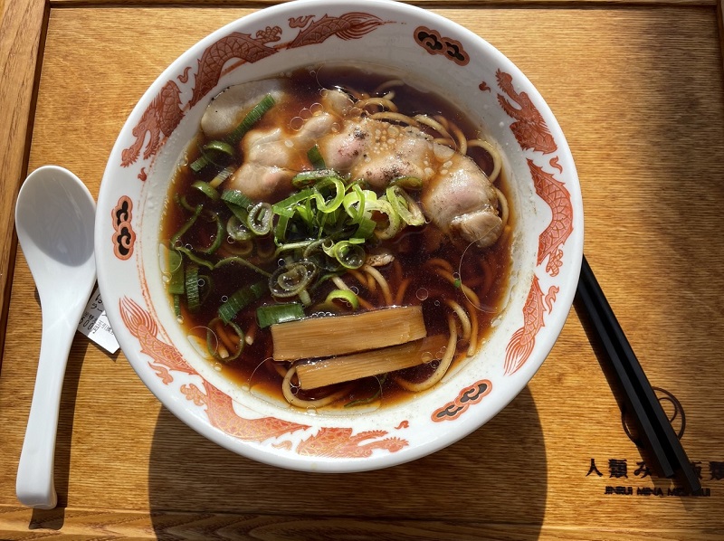 A bowl of ramen with meat and vegetables on a wooden tray
