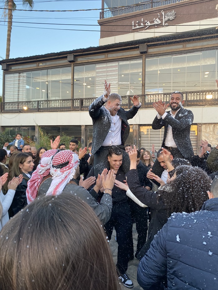 Many Jordanian college graduates and their families celebrating and clapping in a parking lot 