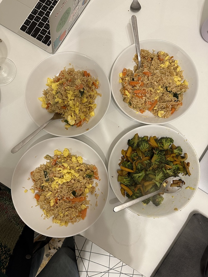 Three bowls of fried rice and a bowl of vegetables on the side, set on a white table with a laptop in the corner.
