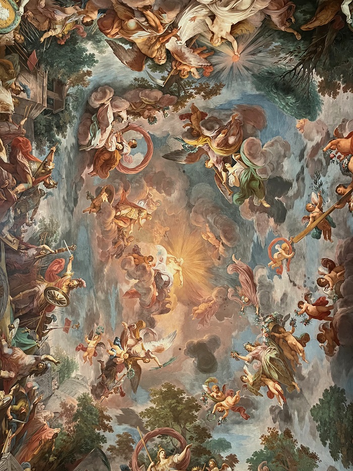 A painting on a ceiling in the Borghese Gallery of angles, warriors with swords and shields, and people on clouds.