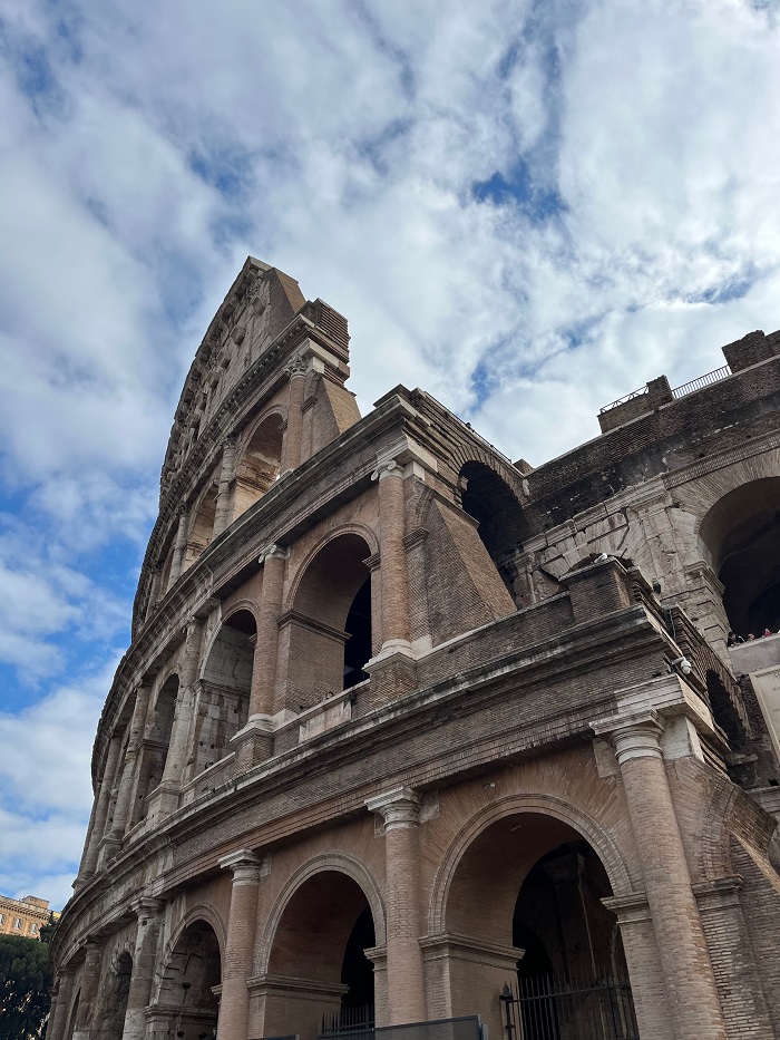 The side of the Colosseum in Rome, Italy beneath bright blue skies with clouds