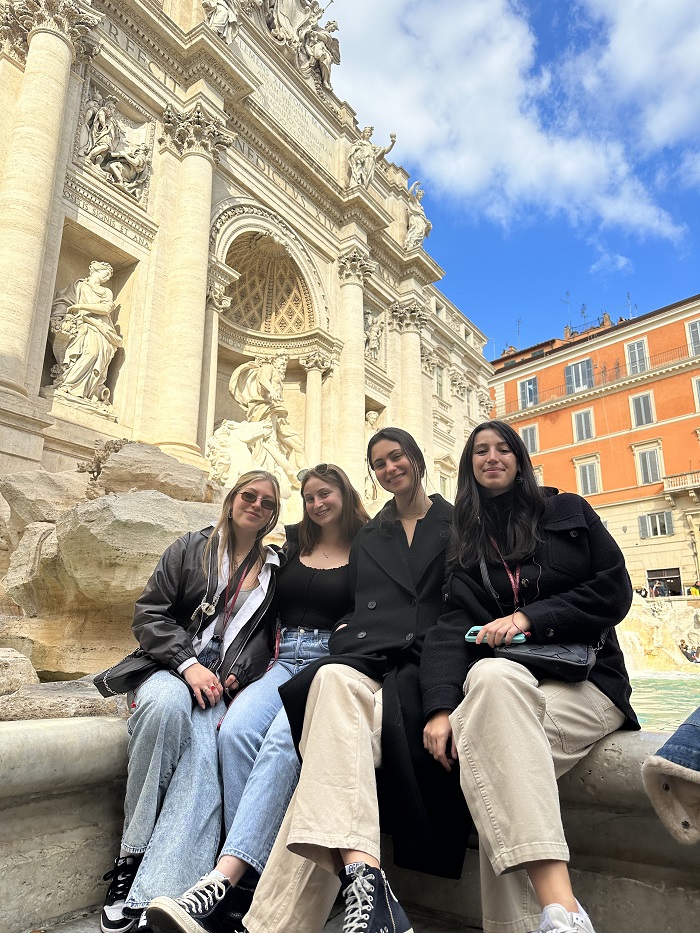 Four CET Florence students smiling while sitting along the edge of the Trevi Fountain in Rome, Italy