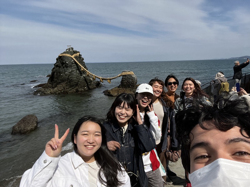 Group photo of seven people in front of the ocean and Meoto Iwa in Mie
