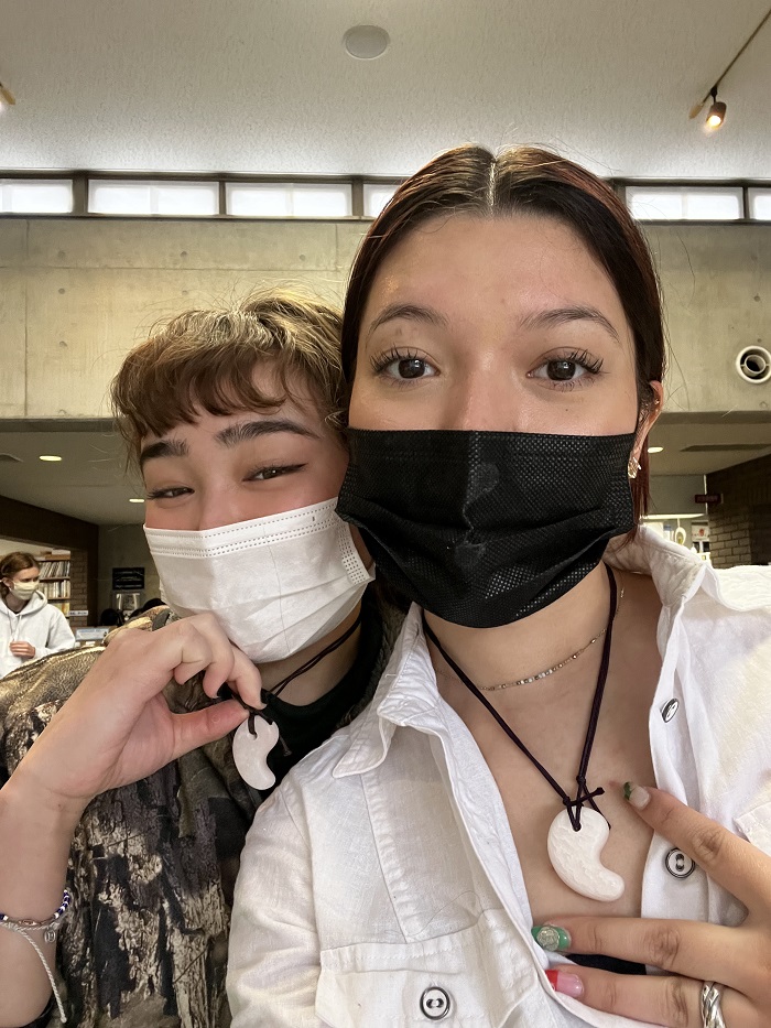 Two CET Japan students taking a selfie while wearing masks and Pink magatama necklaces