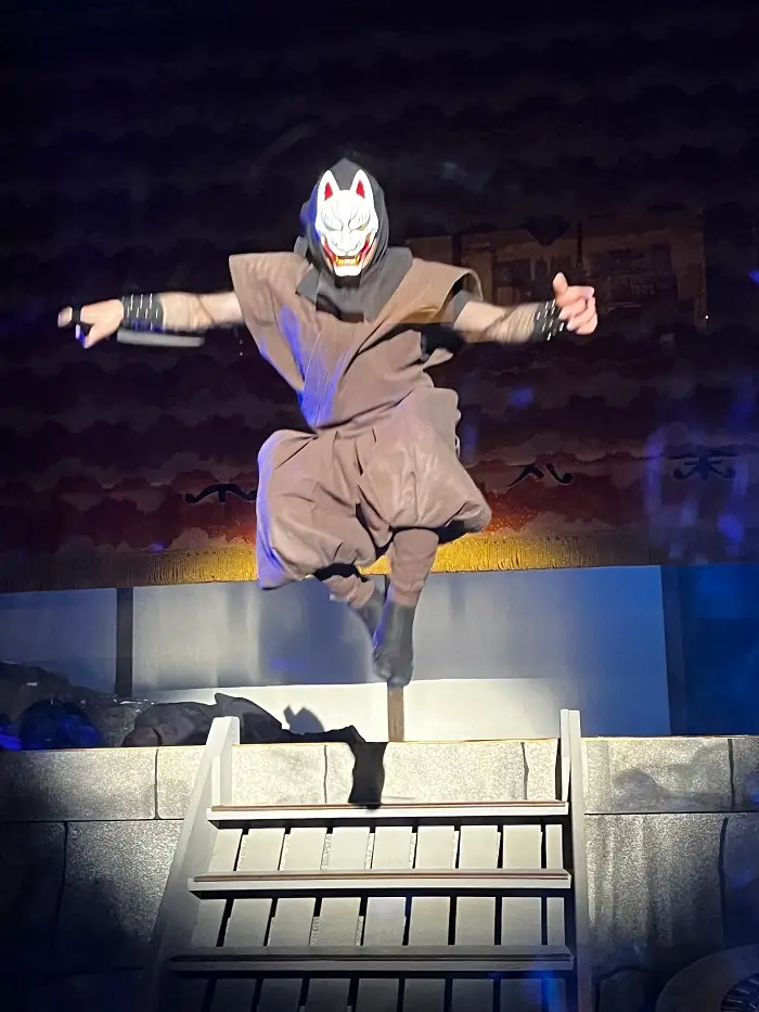 Samurai with a red and white mask in jumping mid-air while holding a sword during a samurai show