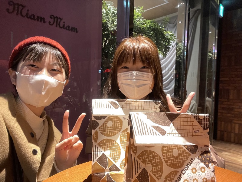 A CET Japan student and OGU student smiling with masks on and with a bag of donuts in front of them at a café
